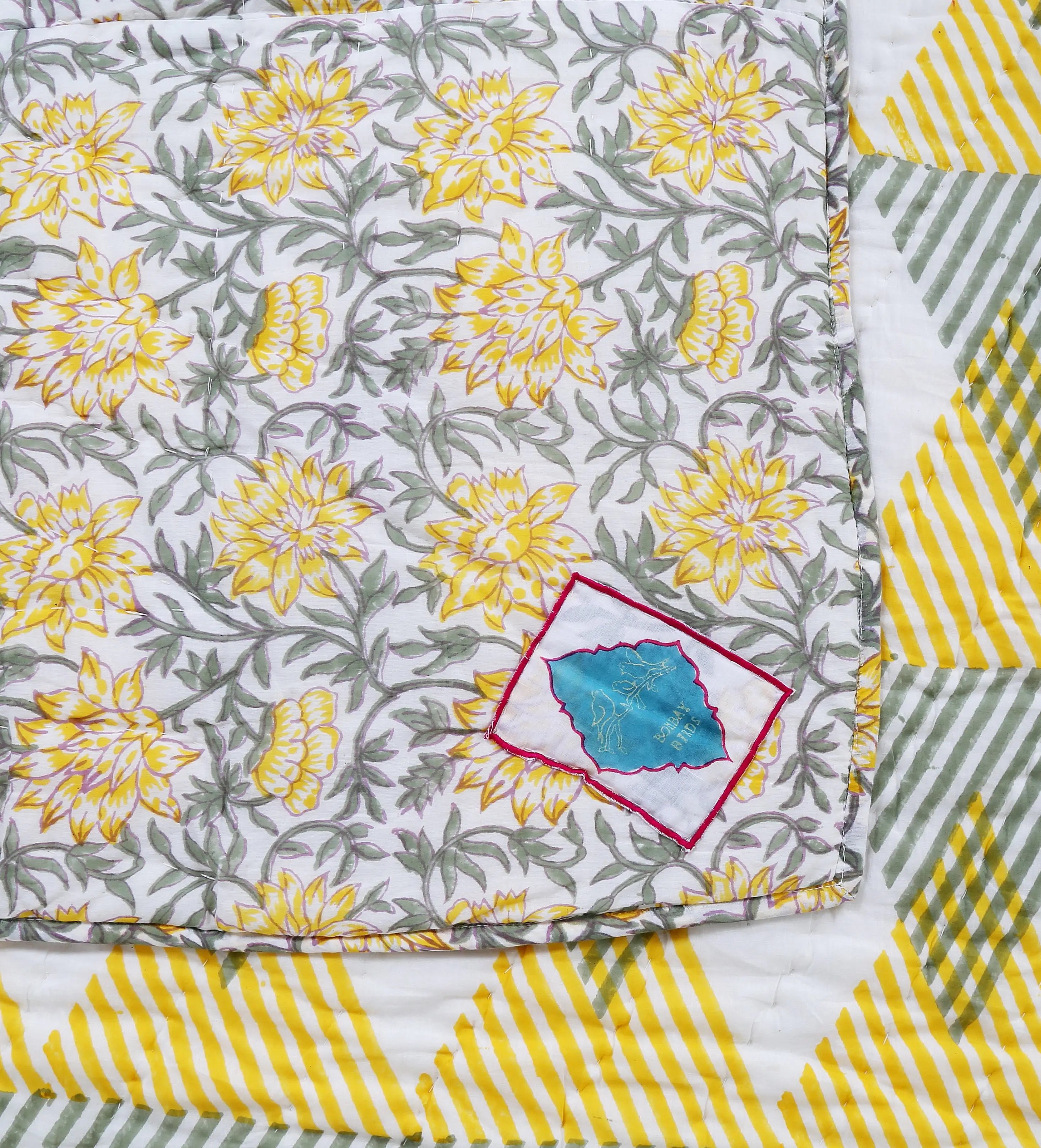 Reversible Sunnie chintz quilt by Bombaybirds featuring floral patterns, displayed on a living room bed or sofa.