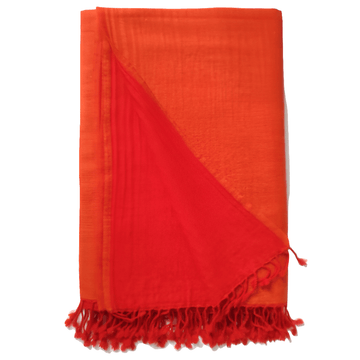 Flamed tangerine Bombaybirds living throw blanket draped over a couch, showcasing vibrant orange and fiery patterned fabric.