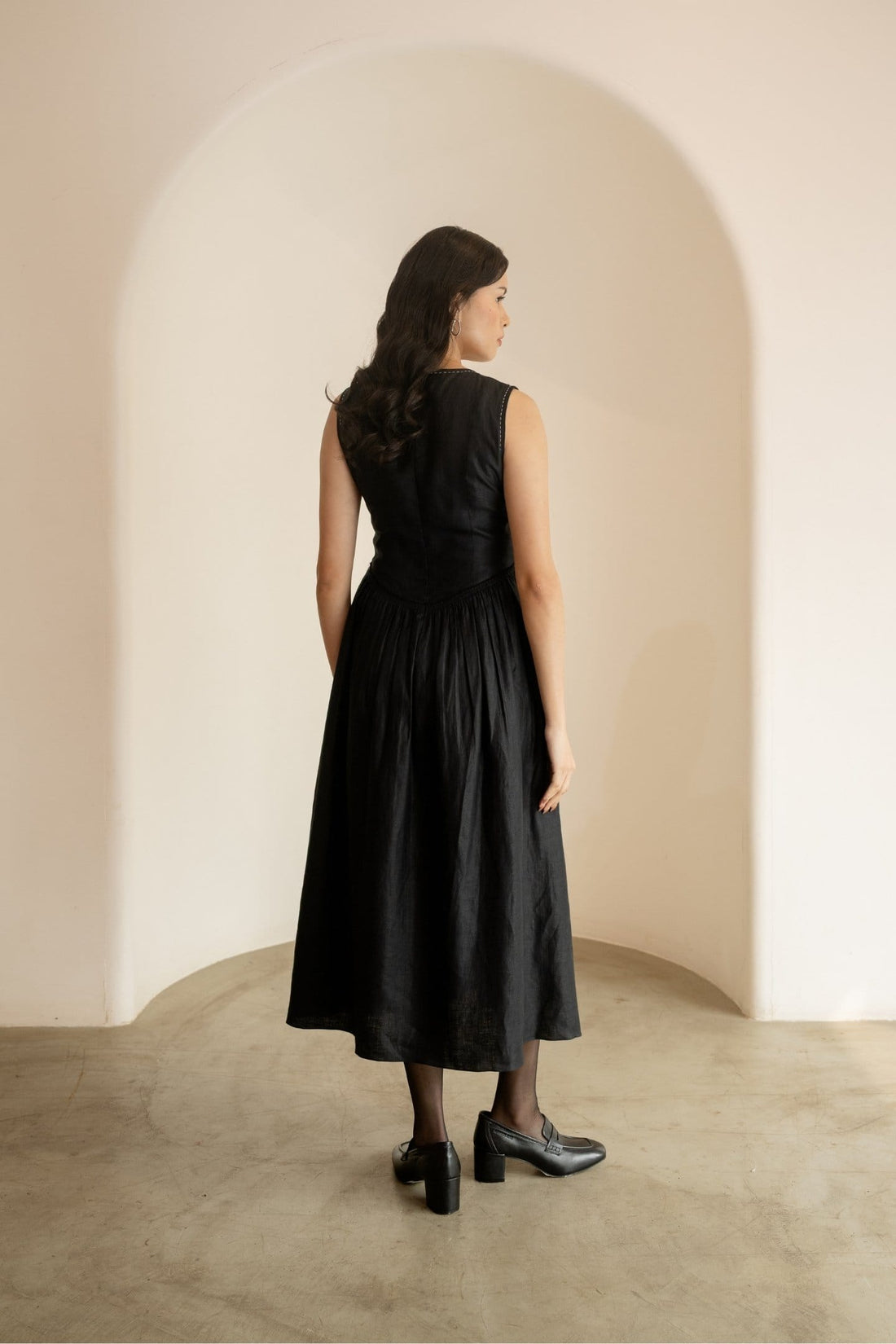 Ebony black sleeveless maxi dress by Alternative, flowing midi length with a fitted waist and elegant round neckline.