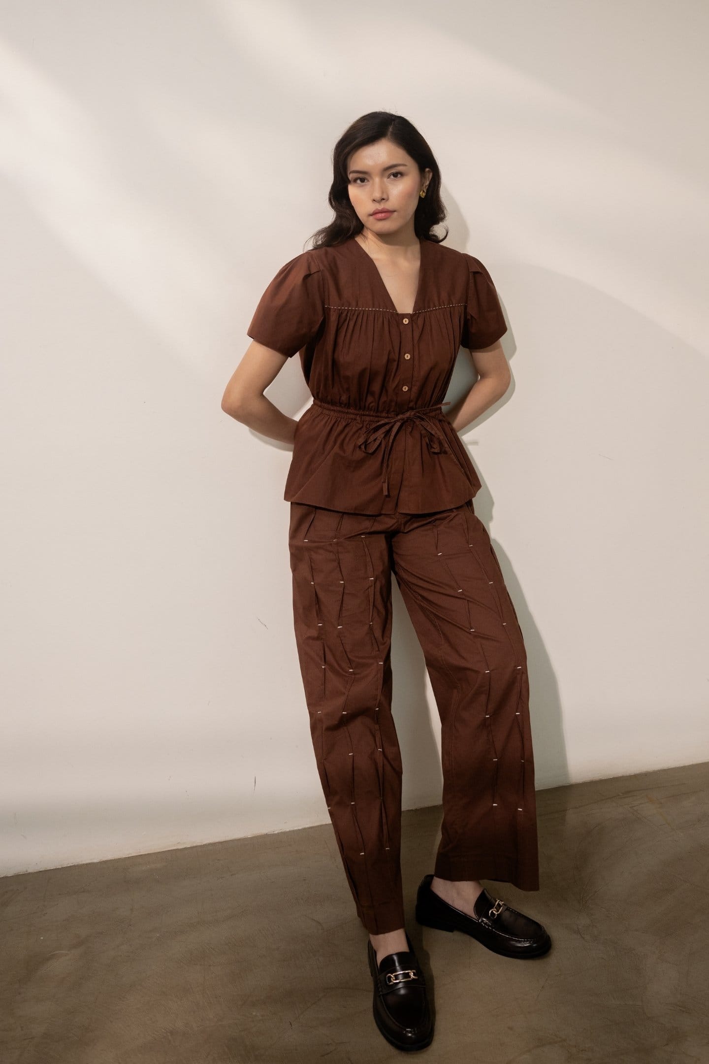 Brown pleated trousers by Alternative, featuring a tie-up waist and relaxed fit, styled with a matching top.