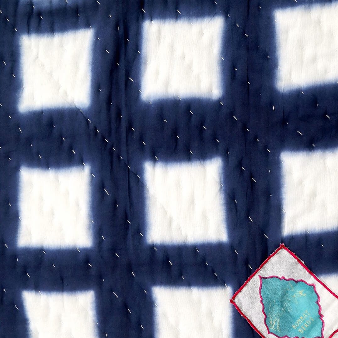 Indigo Shyburi quilt with batik raster pattern in blue and white, displayed on a living space, by Bombaybirds.