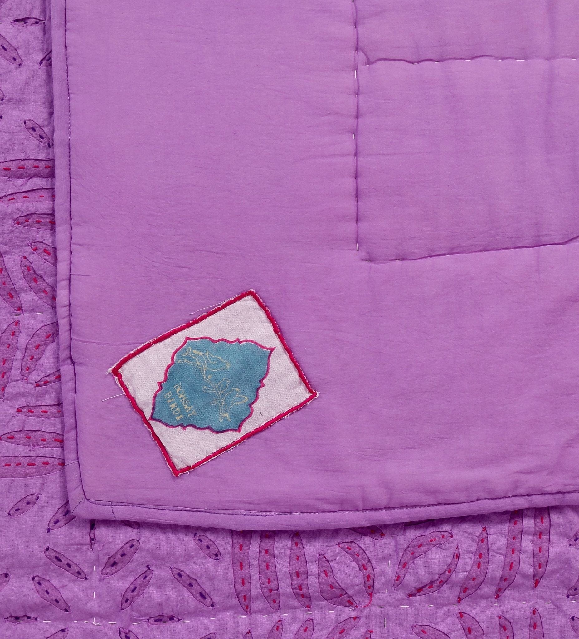 Violet quilt applique on a living room bed by Bombaybirds, made of soft cotton with intricate stitching.