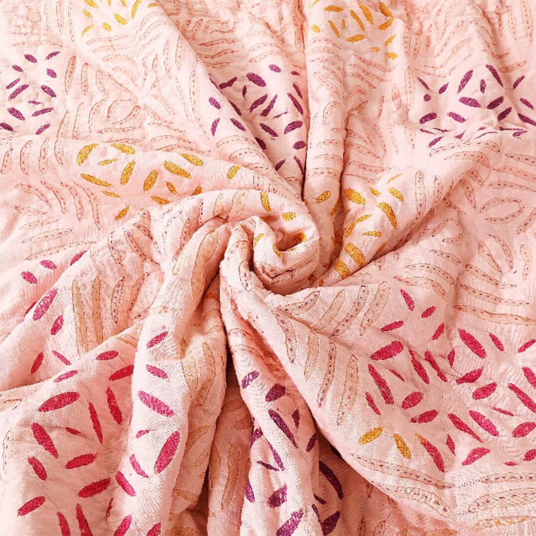 Close-up of Bombaybirds applique blush quilt with textured cotton fabric in soft peach and apricot tones.