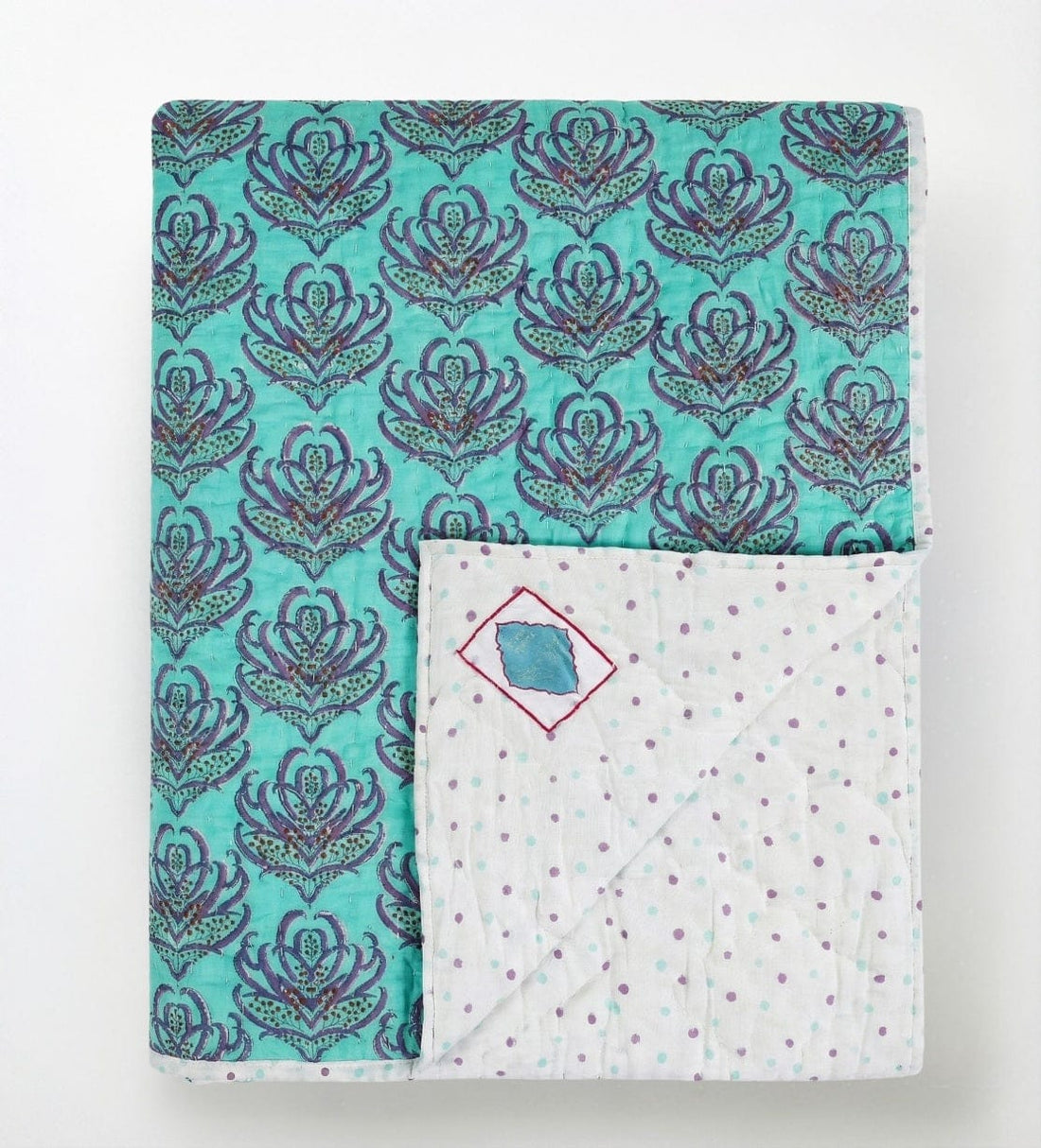 Pink lotus reversible quilt from Bombaybirds, showcasing vibrant pink and turquoise lotus blockprint fabric on a cozy living quilt.