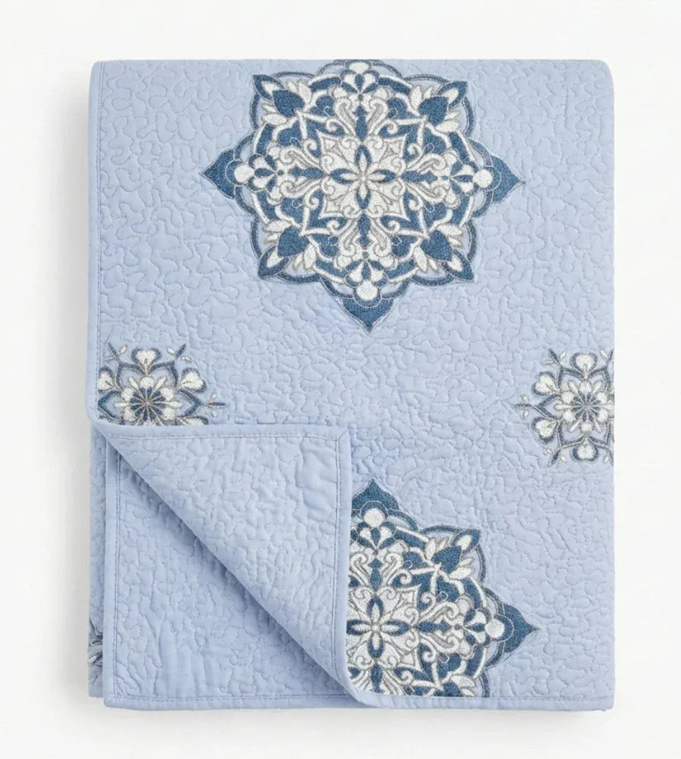 Close-up of the lilac Suzani quilt from Bombaybirds, featuring intricate blue embroidery and detailed floral patterns.