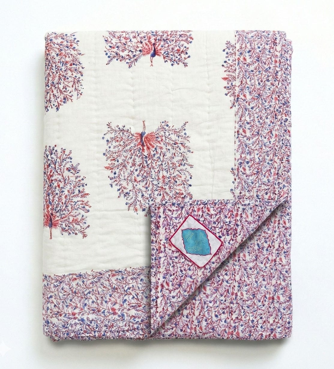 Reversible quilt with peacock feather design by Bombaybirds, featuring contrasting white and vibrant peacock feather patterns.